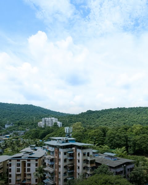 Neelkanth building under a clear sky, surrounded by green mountains.